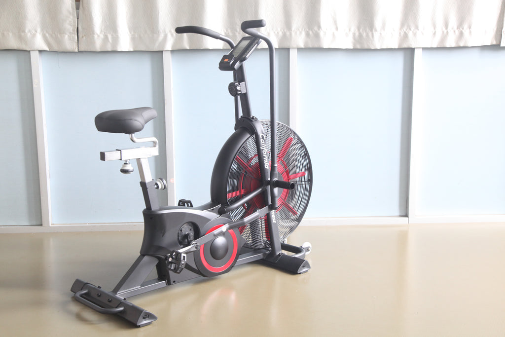 Black and red stationary air exercise bike with large fan wheel, digital display, and padded seat, on light background