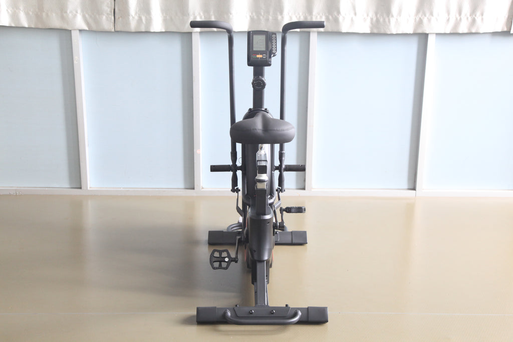 Black upright exercise bike with digital display console, padded seat, handlebars, and pedals with foot straps, front view on