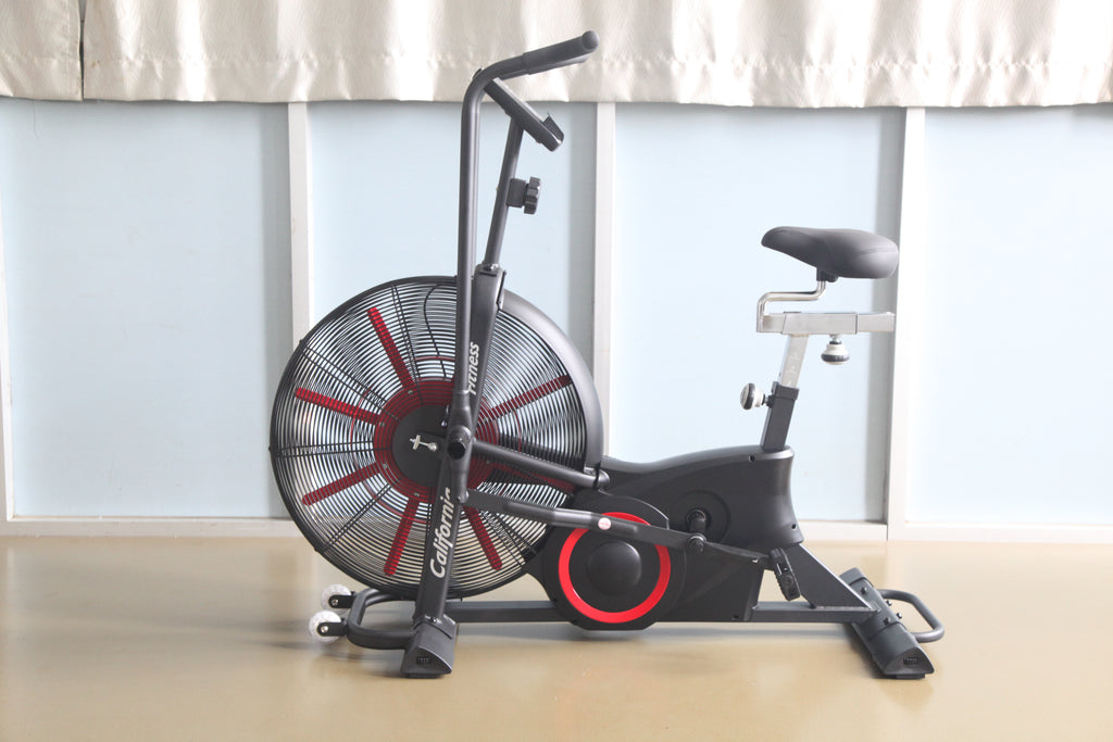 Black and red air exercise bike with large fan wheel, upright handlebar, and padded seat on wood floor