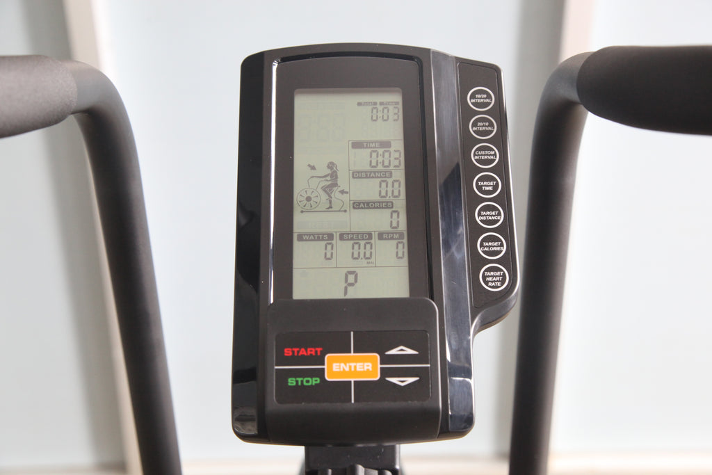 Black stationary exercise bike console with LCD display showing time, distance, calories, watts, speed, and RPM, with gray ha