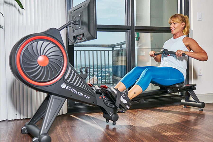Echelon Row-s connected rowing machine with red accents, large fan wheel, and digital display, shown with woman exercising in