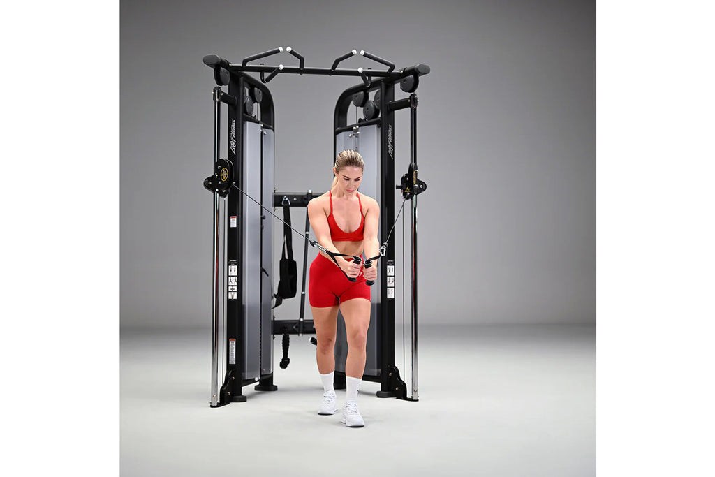 Woman in red sports bra and shorts using black and silver dual adjustable pulley machine on gray background