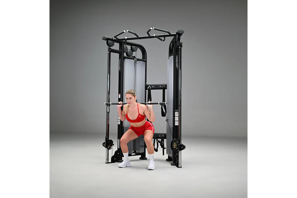Woman in red sports bra and shorts using black dual adjustable pulley cable machine on gray background