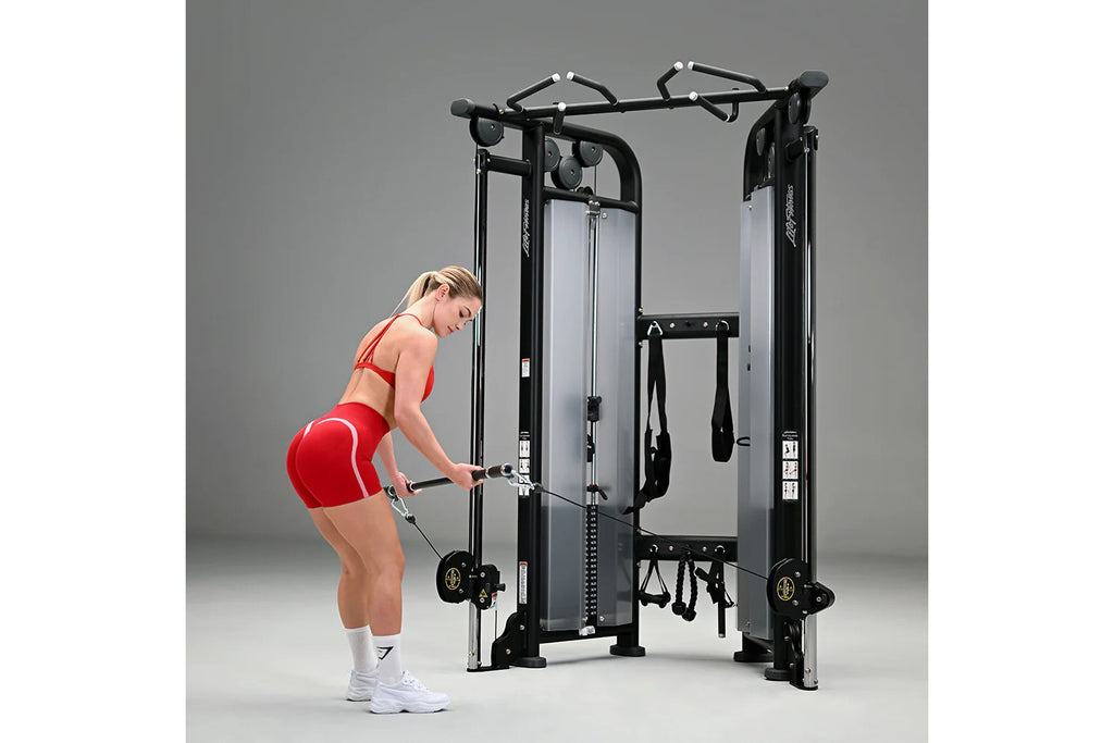 Black and silver dual adjustable pulley machine with cable attachments, worn by model in red sports bra and shorts on gray ba