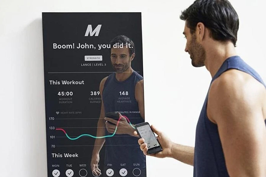 Man wearing blue tank top viewing lululemon Studio Mirror displaying workout metrics and heart rate data on black screen