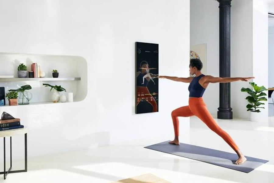 Woman in navy sports bra and orange leggings performing yoga pose in front of black rectangular mirror mounted on white wall